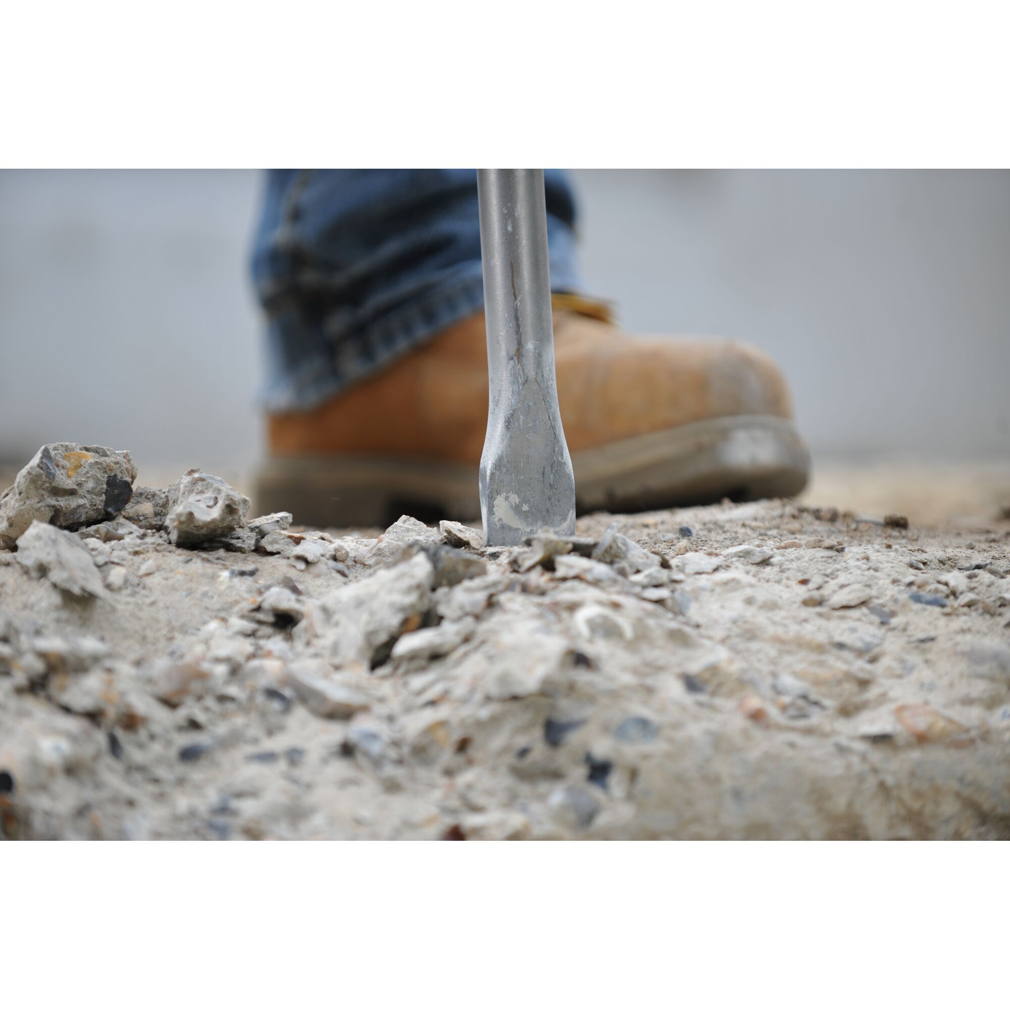 Close-up of a demolition tool breaking concrete on the ground, with a person wearing work boots in the background.