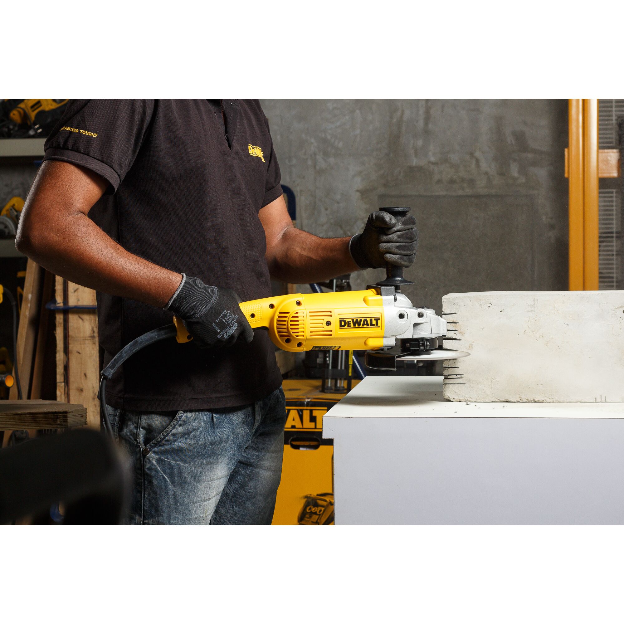 A person wearing gloves uses a yellow DEWALT angle grinder (SKU: D28413) to cut grooves into a concrete block on a worktable in a workshop environment.