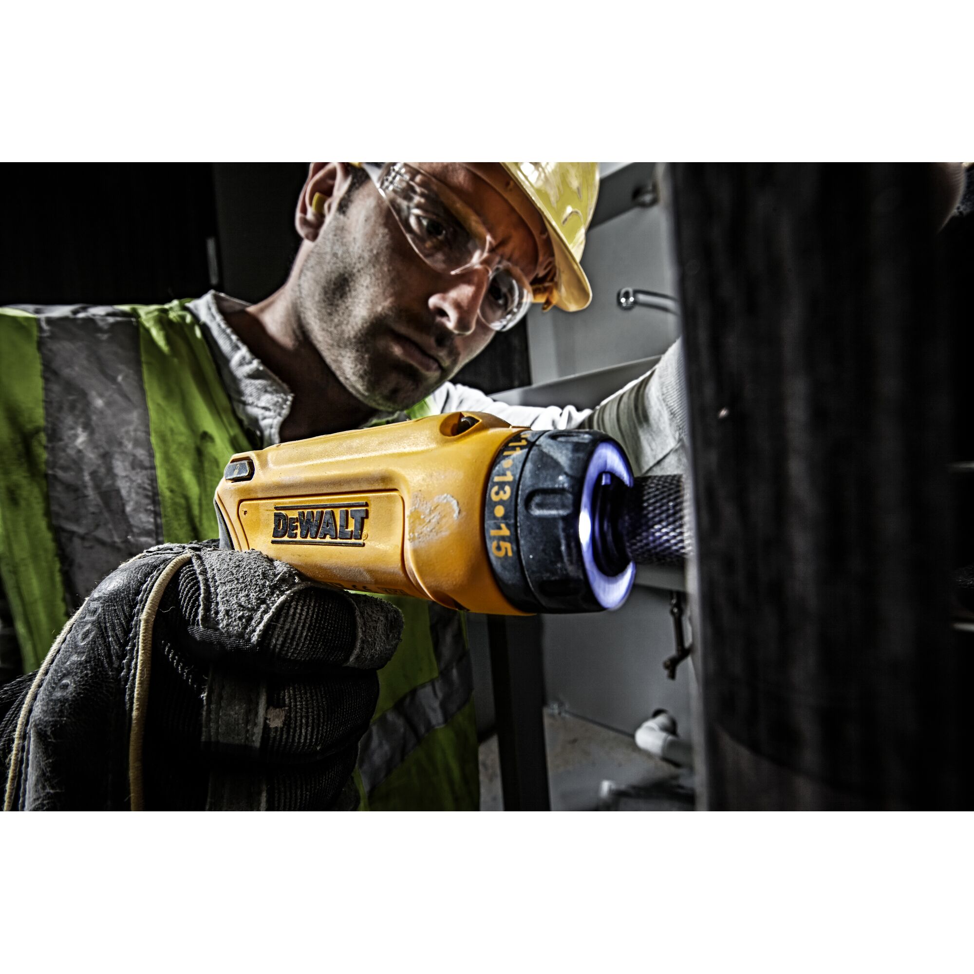 A person wearing a reflective safety vest and gloves uses a yellow DEWALT cordless screwdriver (model DCF680G2) for maintenance work indoors. The focus is on the tool and the user's gloved hand. The person's face is blurred for privacy.