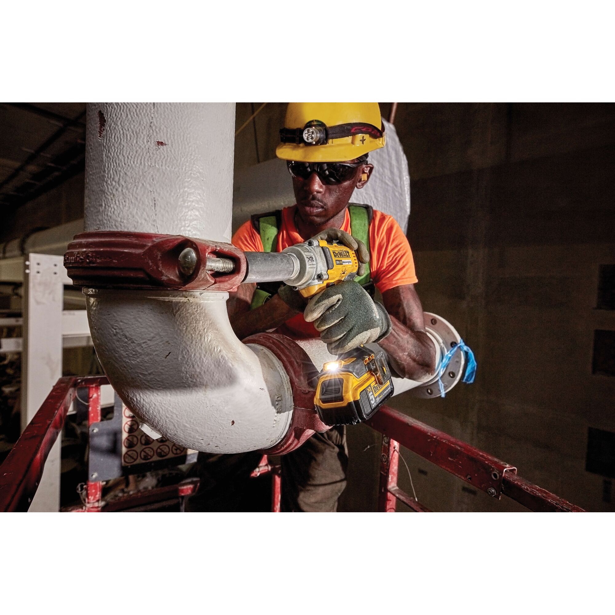 Photo of worker using DEWALT impact wrench DCF894P2 on industrial pipe in construction setting.