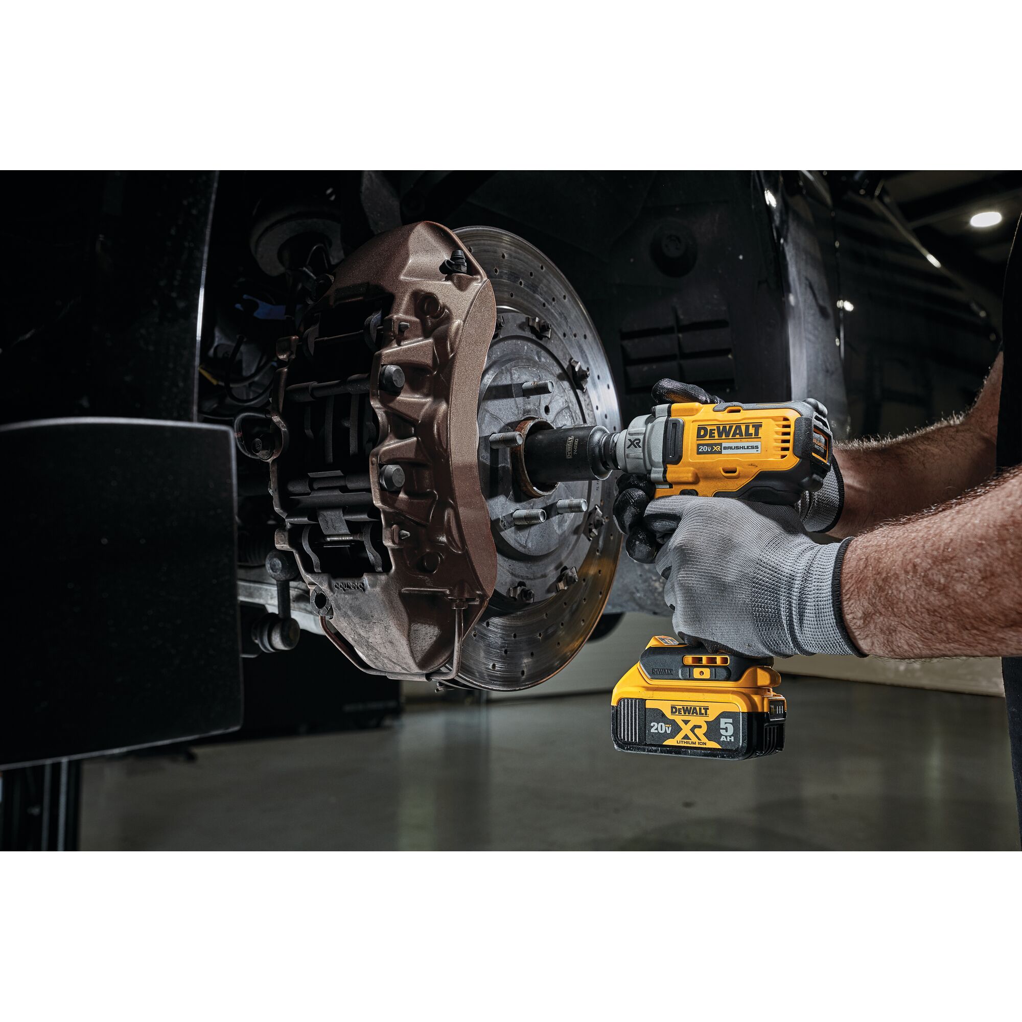 A person wearing gray gloves uses a DEWALT 20V cordless impact wrench to work on a car's brake rotor and caliper assembly.