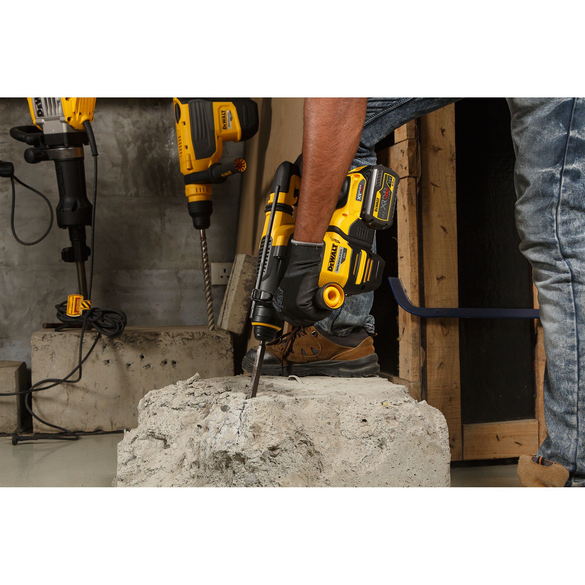 A person using a DEWALT DCH333NT cordless rotary hammer to drill into a concrete block. The worker is wearing gloves and work boots, and other DEWALT power tools are visible in the background.