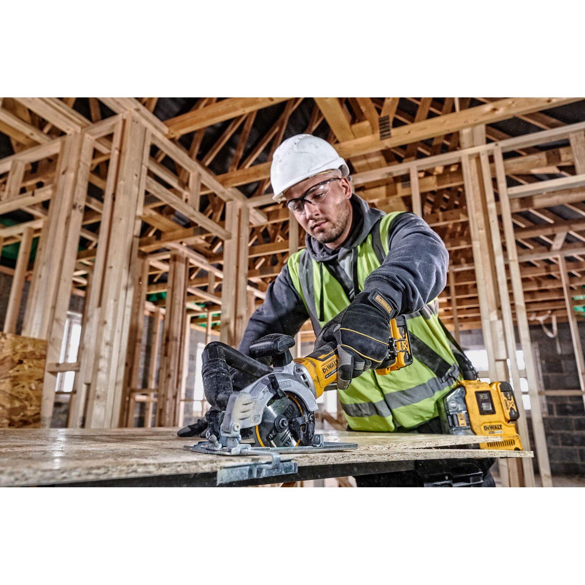 Worker uses a DEWALT circular saw to cut wood at a construction site, wearing safety gear and a helmet.