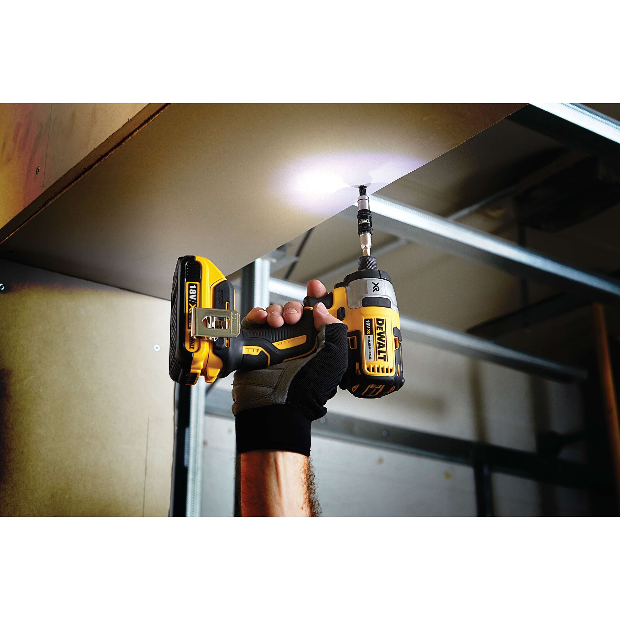 A person wearing a glove uses a DEWALT cordless power drill to drive a screw into an overhead surface. The drill has an LED light illuminating the work area.