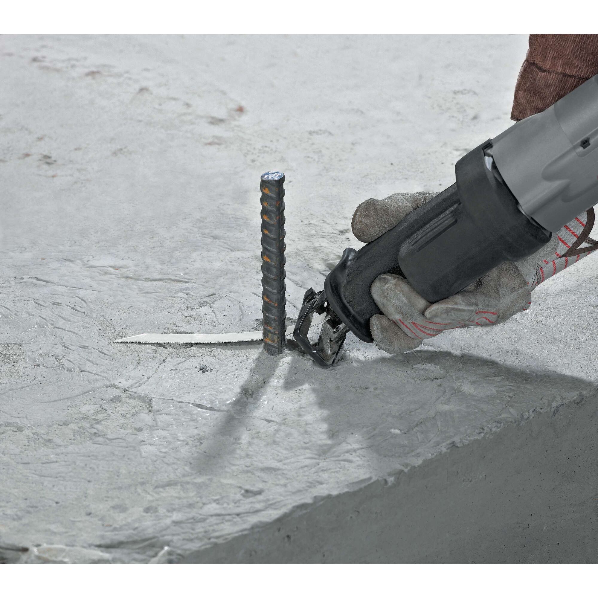 A gloved hand using a DEWALT reciprocating saw to cut through a metal rebar embedded in a concrete surface.