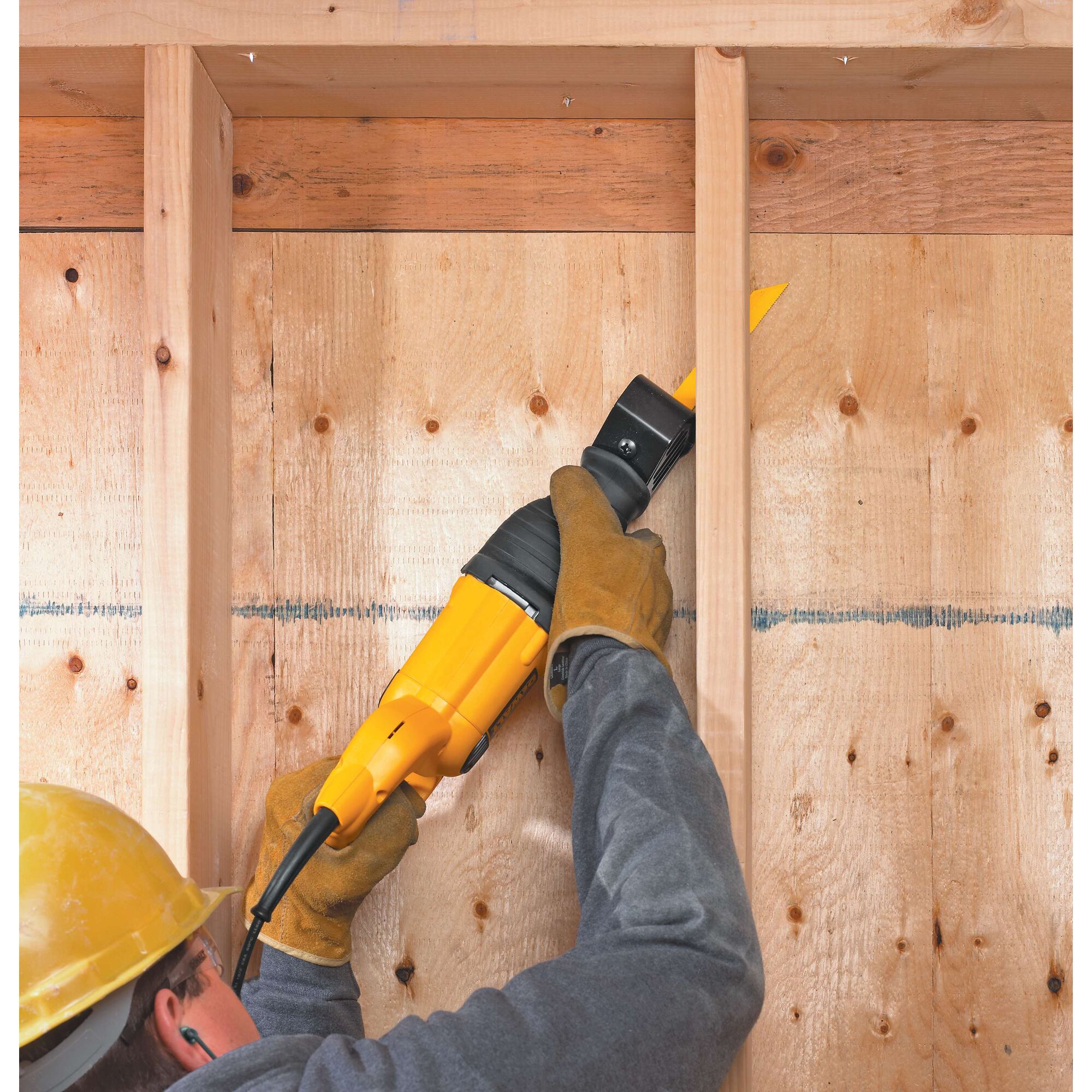A person wearing gloves and a yellow hard hat uses a yellow DEWALT reciprocating saw to cut wooden beams in a construction setting.