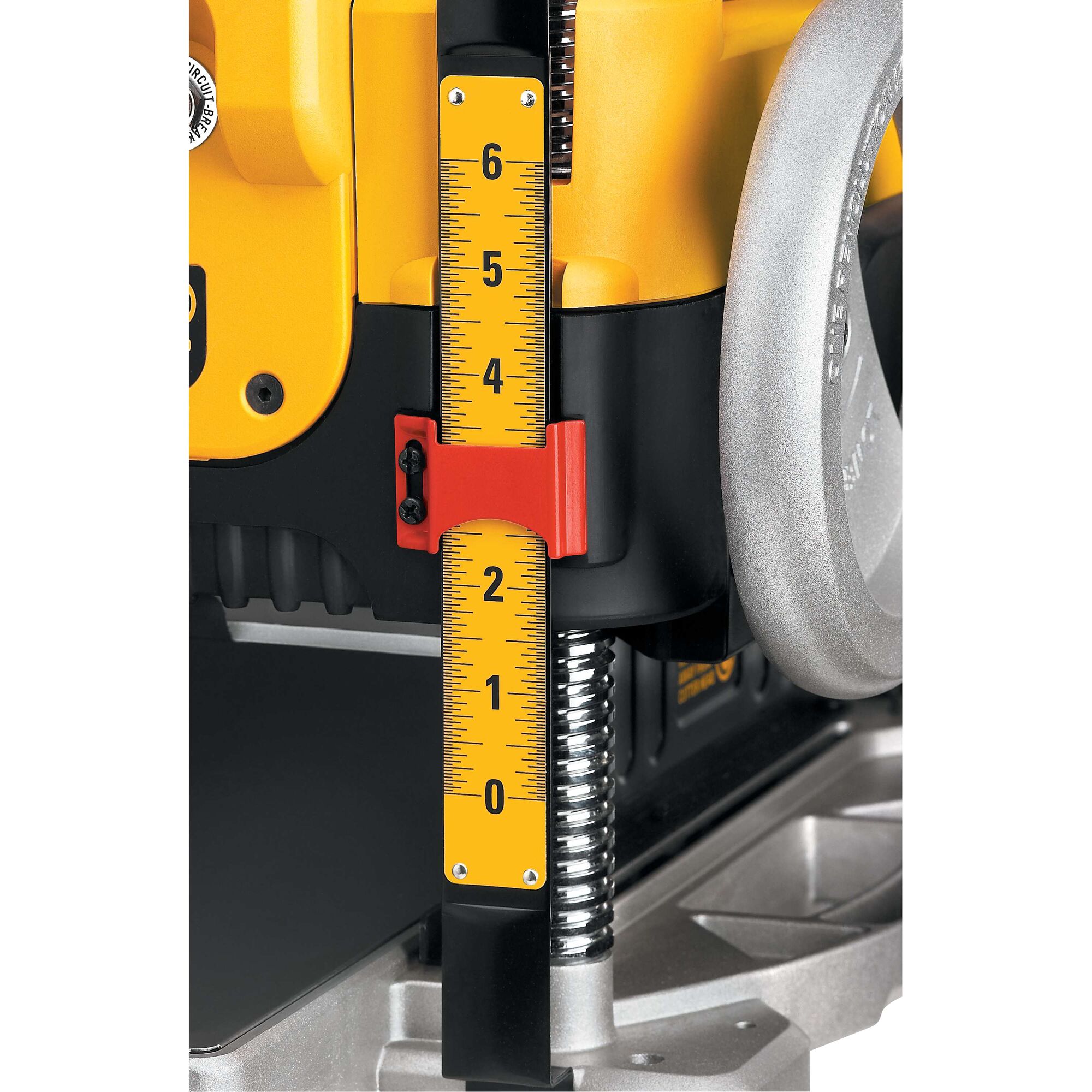Close-up view of a yellow measuring scale with black markings and numbers, attached to a DEWALT machine. The scale has a red adjustable marker and is mounted beside a silver hand wheel and metal spring.