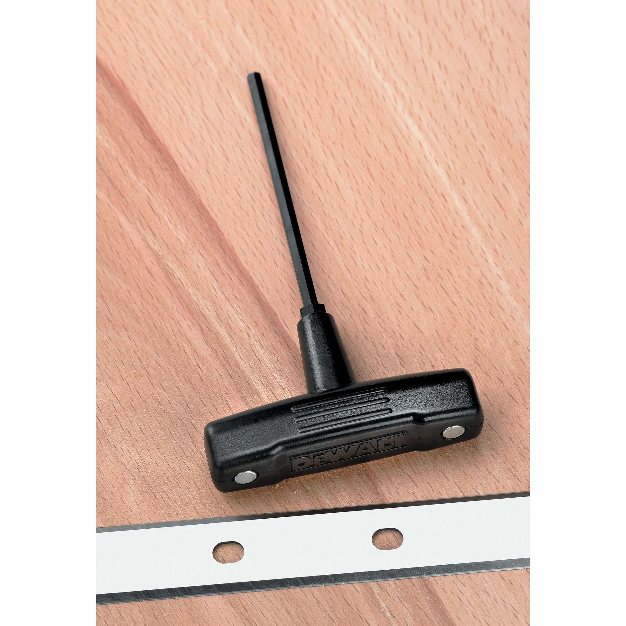 A DEWALT branded T-handle hex key tool placed on a wooden surface, next to a metal strip with holes.