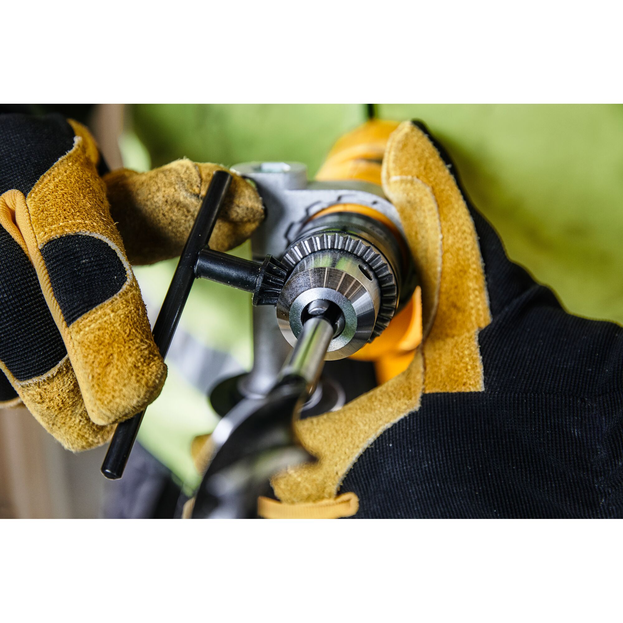 Close-up of a person wearing work gloves using a chuck key to tighten a drill bit in a DEWALT power drill.