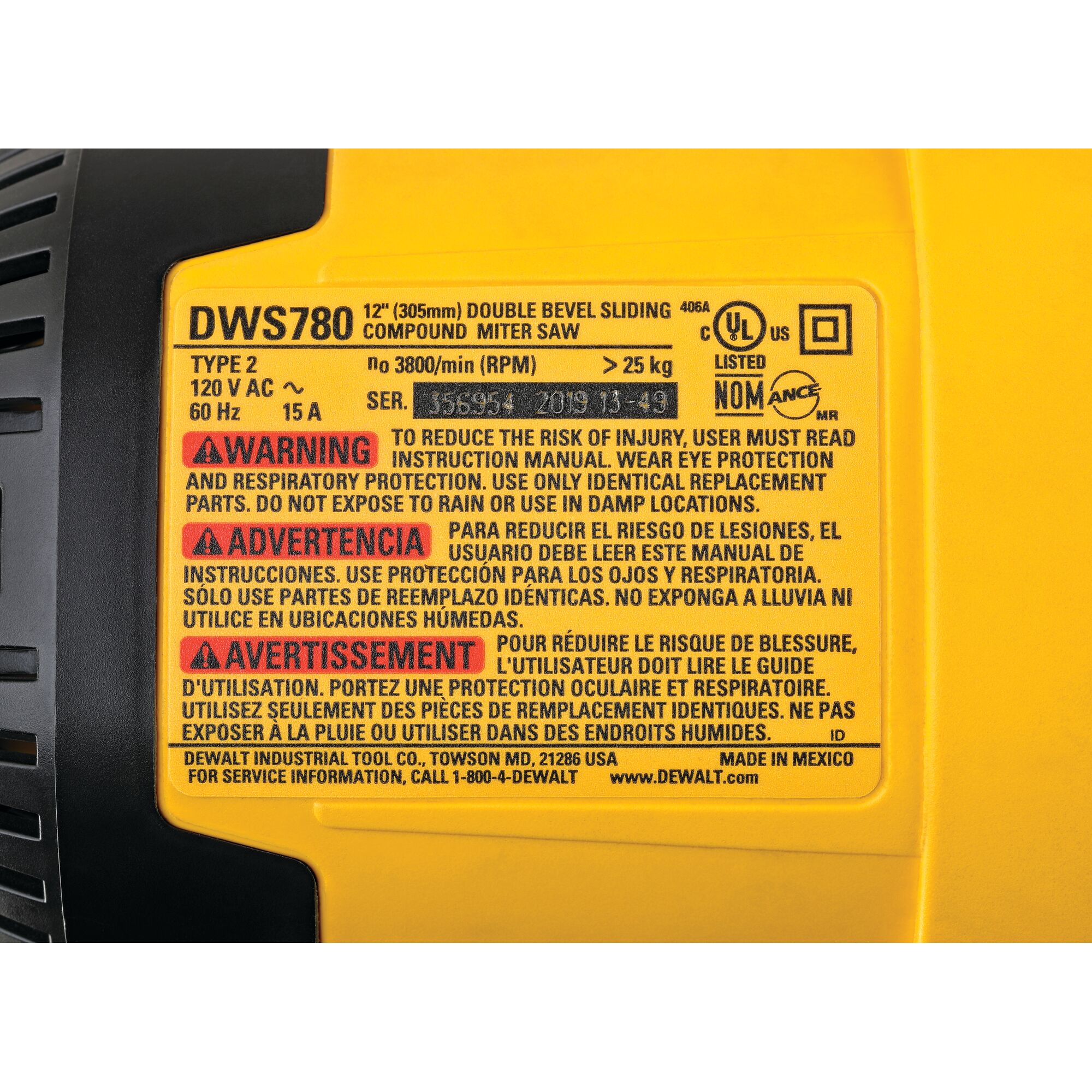 Close-up image of the yellow product label on a DEWALT DWS780 12-inch double bevel sliding compound miter saw. The label displays specifications such as 120V AC, 60Hz, 15A, more than 25 kg weight, and 3800 RPM. It contains warnings in English, Spanish, and French about safety precautions including reading instructions, wearing eye and respiratory protection, using identical replacement parts, and not exposing the tool to rain or damp locations. Certification and service information are also present.