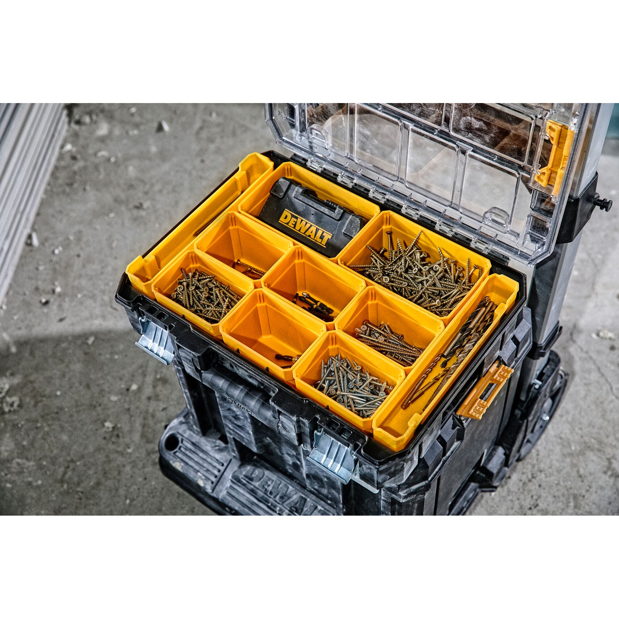A DEWALT portable storage organizer with yellow compartments holding various screws and hardware is shown open, sitting on a construction site floor.