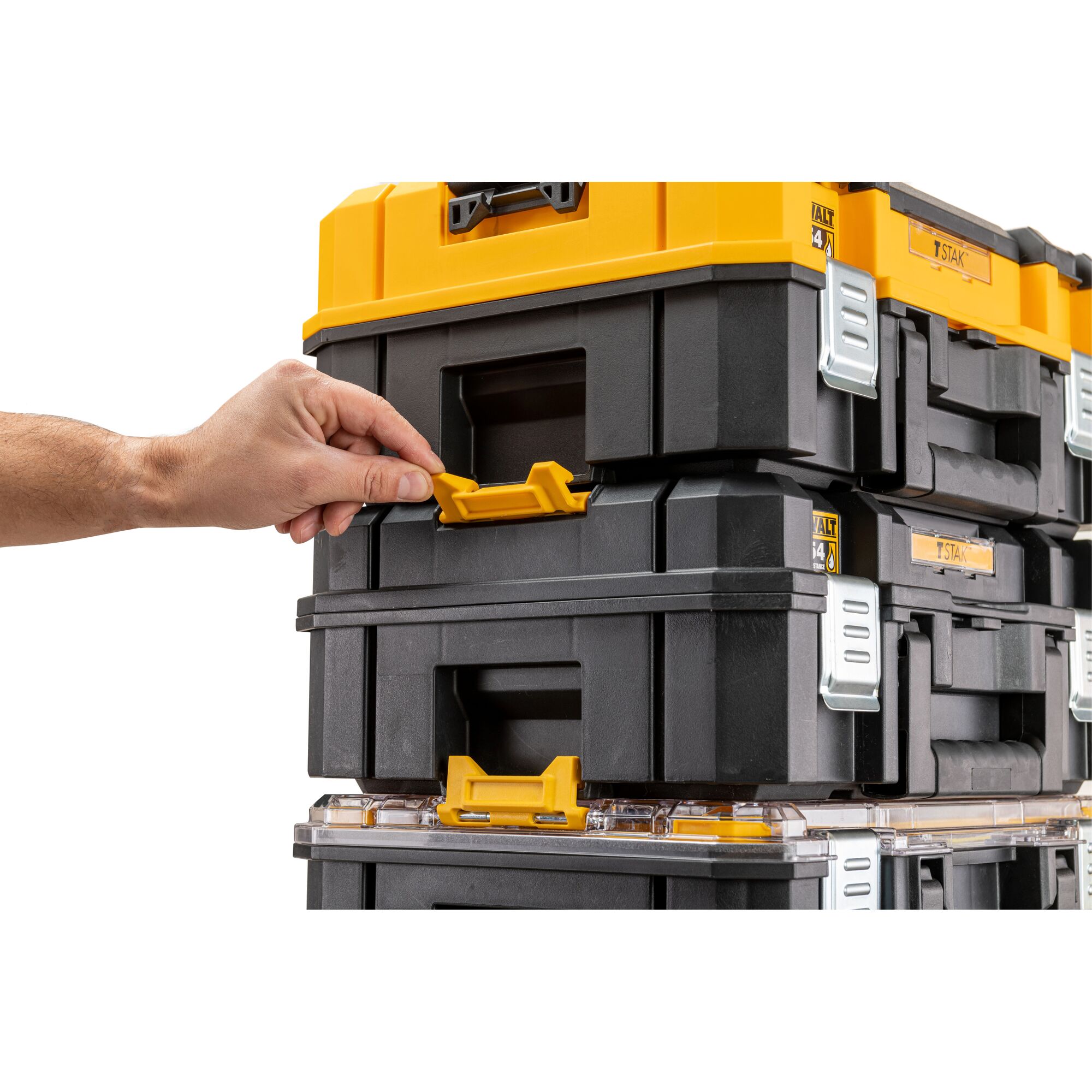 A hand is adjusting the yellow latch on a stack of DEWALT TSTAK modular storage boxes. The boxes are black with yellow and silver details.