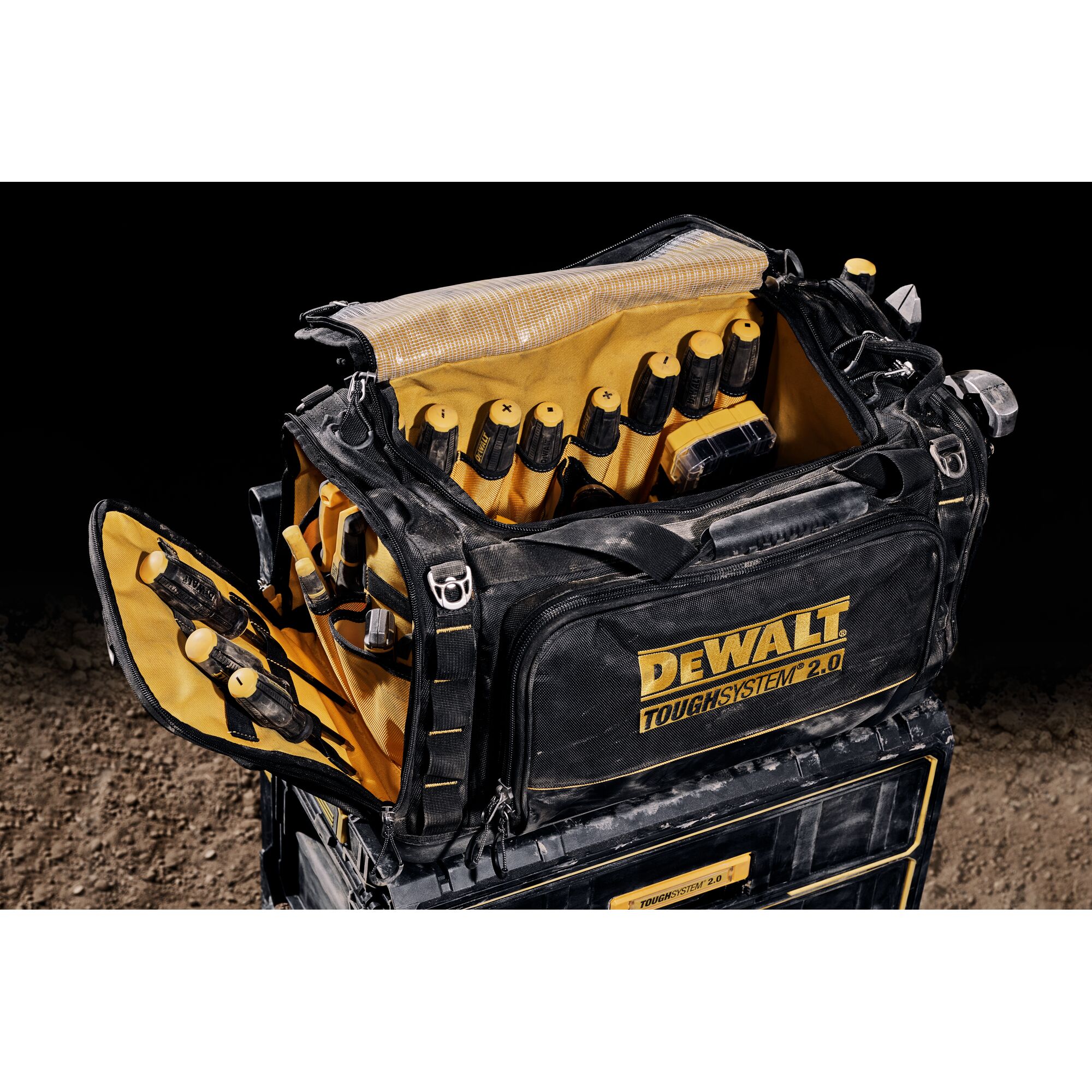 A DEWALT TOUGHSYSTEM 2.0 black and yellow tool bag is open, showing the interior filled with hand tools organized in pockets. The bag is sitting on top of a matching storage box and is suitable for carrying and organizing tools.
